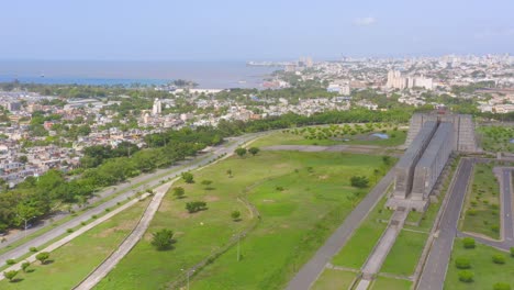 Avance-Aéreo-Sobre-El-Parque-Alrededor-De-Faro-Colón-Y-La-Ciudad-En-El-Fondo,-Santo-Domingo