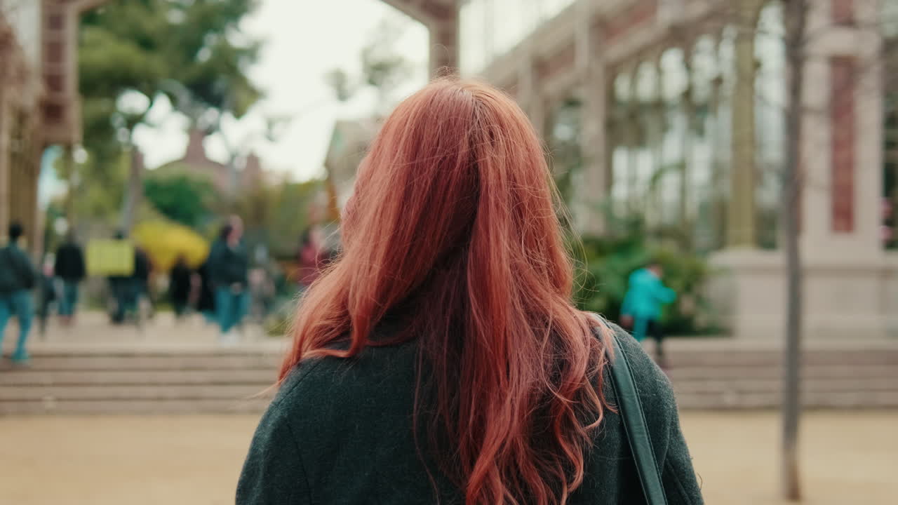 Donna con lunghi capelli rossi che si allontana in un parco cittadino