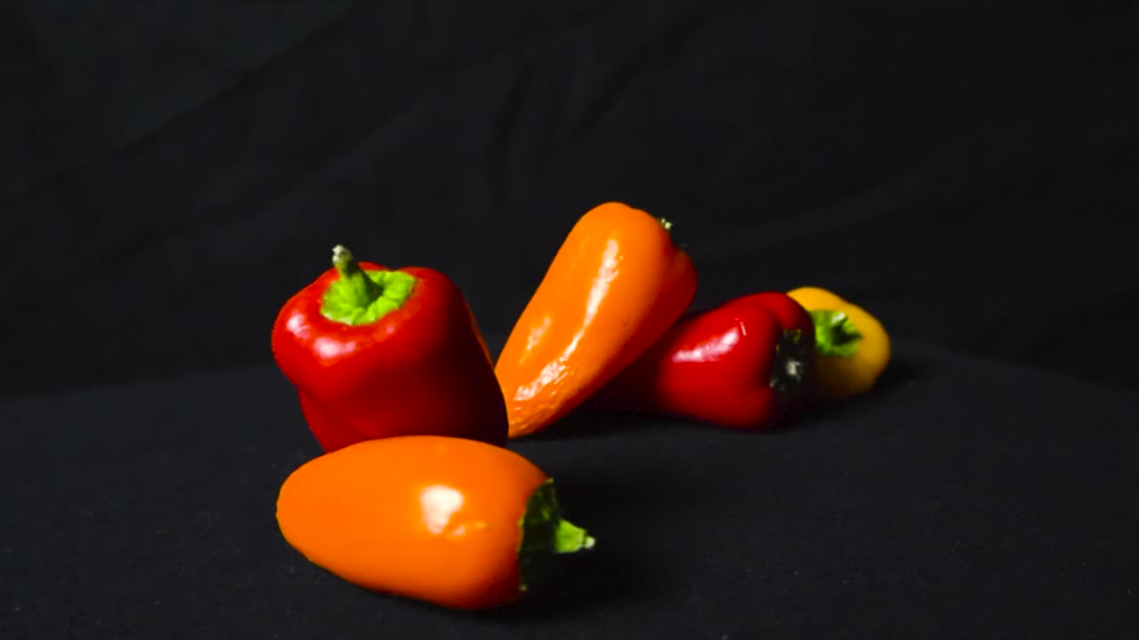 magnífico primer plano o primer plano de colorido rojo, naranja y amarillo pequeño pimentón o fruta fría en un fondo negro oscuro bajo luces de estudio mientras el metraje está haciendo zoom en y sobre ellos lentamente.