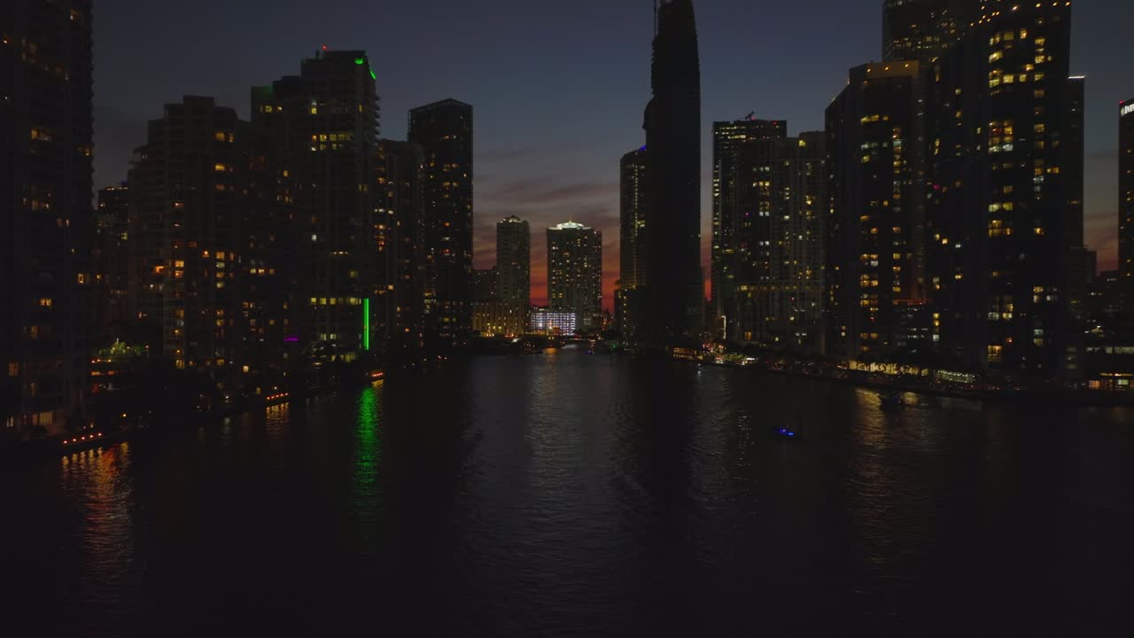 Cinematic evening shot of tall buildings along river. Silhouettes on high rise apartment houses against colourful twilight sky. Miami, USA