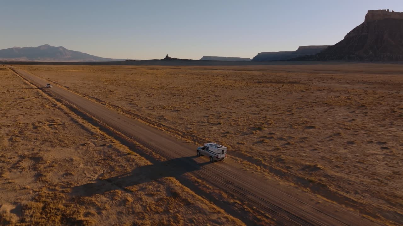 Ripresa aerea media in movimento di un veicolo che attraversa una vasta pianura desertica vicino a Factory Butte, Utah