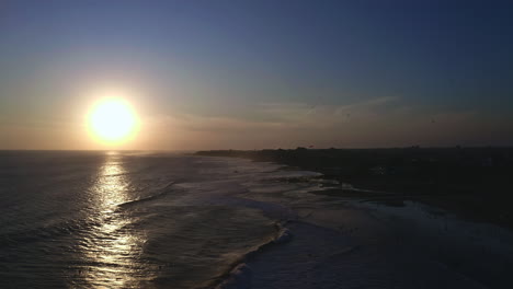 Large-Sun-setting-beyond-ocean-horizon-over-Canggu-beach-at-dusk,-Bali