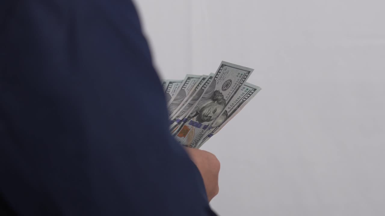 Mano che regge e agita una pila di banconote da cento dollari USA. Primo piano sul conteggio del denaro. Video 4K.