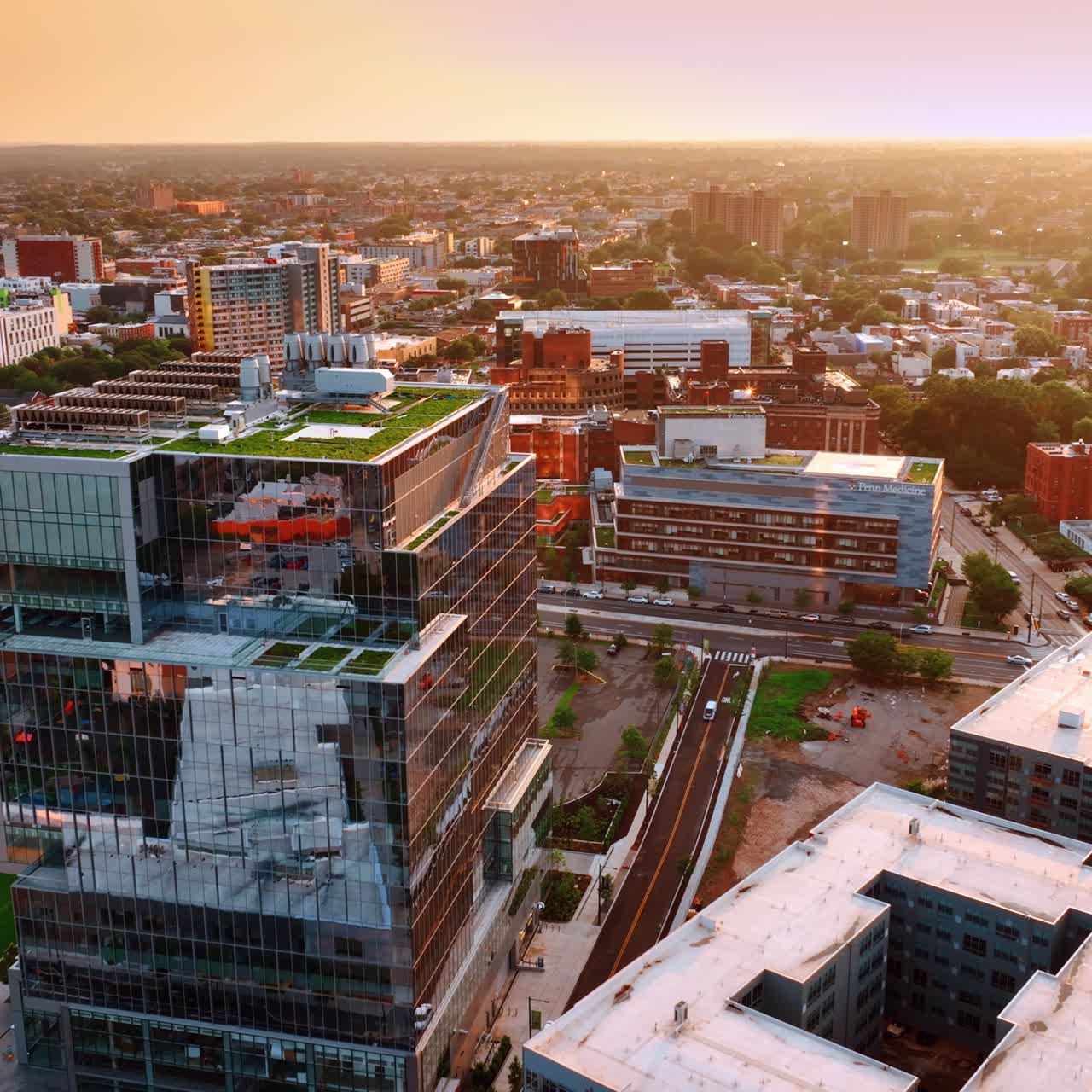 Approaching modern glass building with green zone on top. Philadelphia cityscape from air at sunset