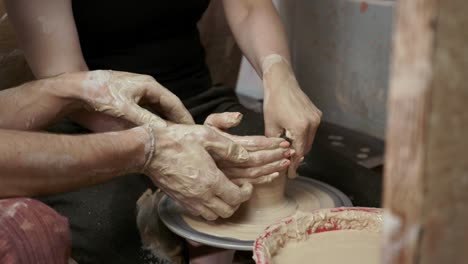 a potter teaches a woman to make clay dishes. a man takes a woman's hands