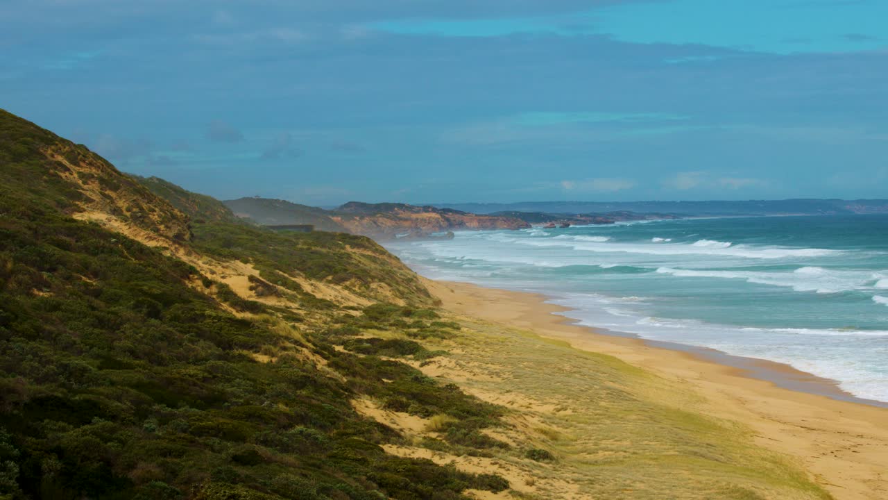 Sweeping aerial shot of limestone cliffs, sandy beach, and rolling ocean waves under daylight