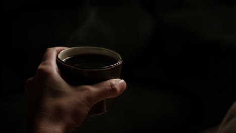 hand holding a steaming cup of coffee in a dark setting