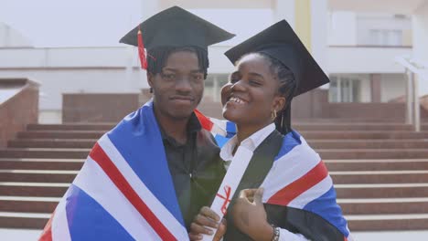 african american man and woman stand side by side facing the camera in black robes and square hats of graduate students with the british flag on their shoulders