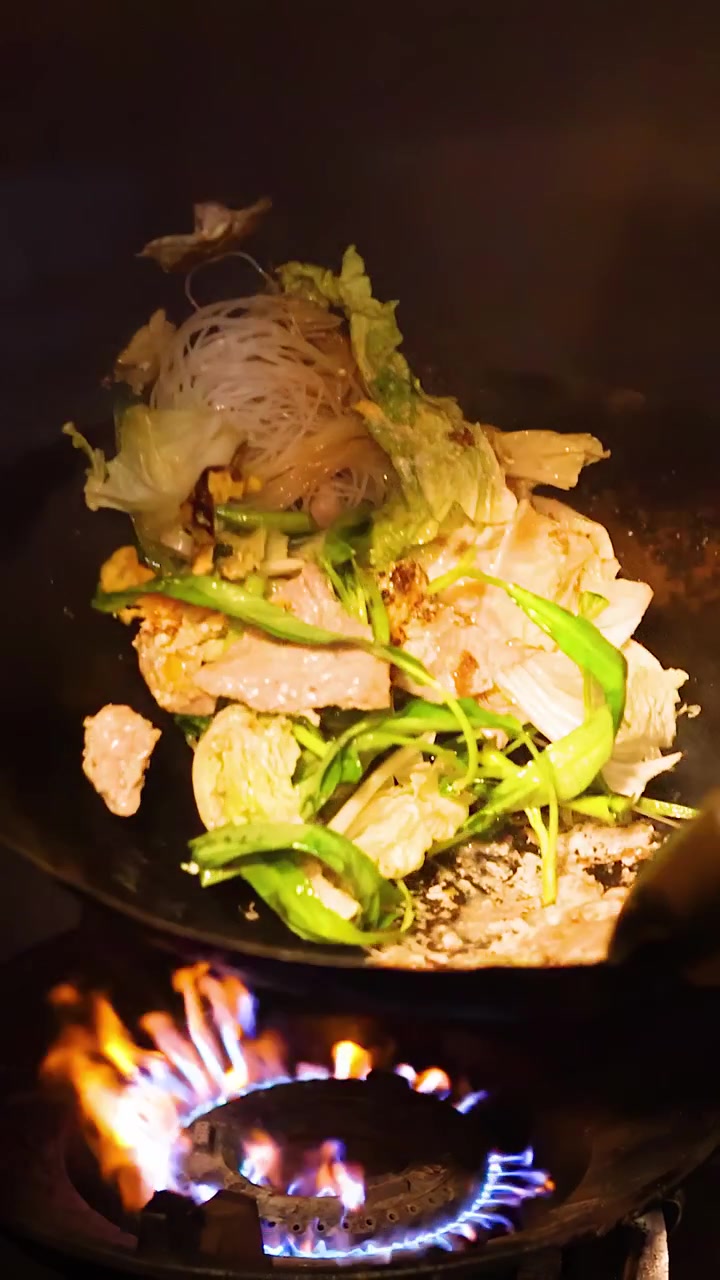 薄暗い照明の中、シェフが炎の上がる中華鍋ですき焼き麺、野菜、肉を炒める