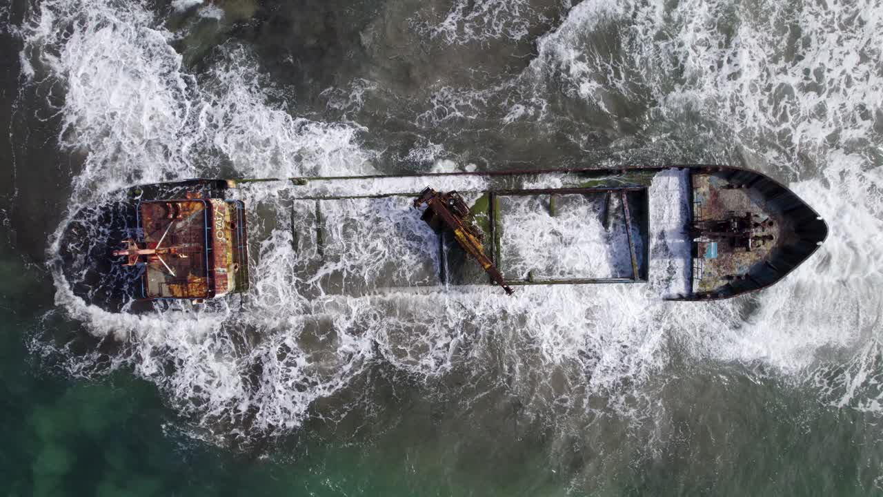 Aerial Birds Eye shot of a shipwreck near Manzanillo, Costa Rica, showcasing the powerful ocean waves and the rusty remains of the ship in the swirling waters.