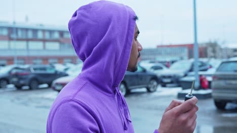 Perspective-shot-of-a-worried-Asian-man-in-purple-hoodie-looking-around-for-his-car-in-parking-lot-with-key-in-hand