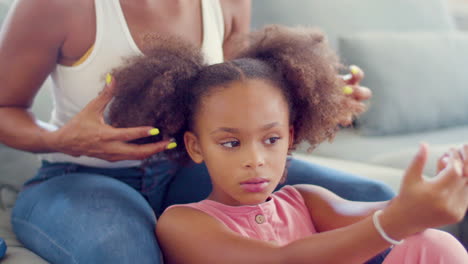 black woman sitting on couch touching her daughters pigtails