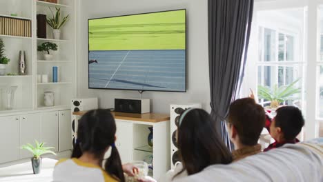 Composite-of-happy-family-sitting-at-home-together-watching-athletics-running-on-tv