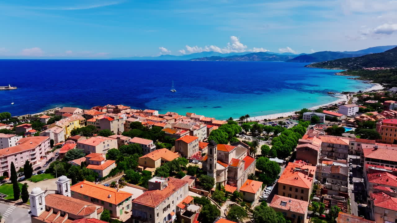 Ripresa aerea con drone sopra la città costiera di Île-Rousse nella regione di Balagne in Corsica, Francia. Vista della spiaggia e del mare turchese in lontananza