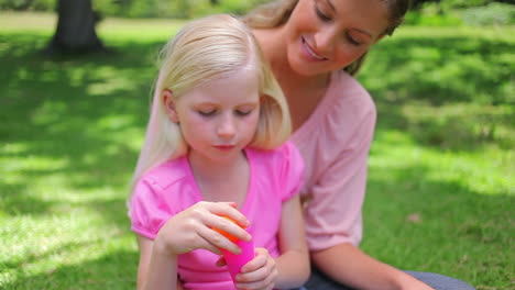 a girl repeatedly blows bubbles with her mother as she sits in the park