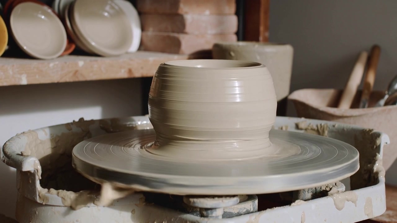 En spinnende dreieskive, våt leirepotte formes og glattes på en studio-dreieskive med stablede skåler og verktøy.