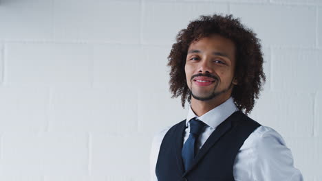 portrait of smiling young businessman wearing suit standing against white studio wall