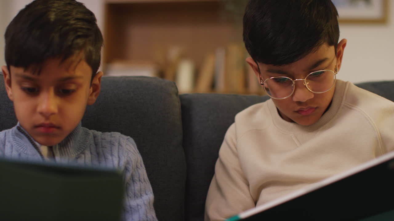 Two Young Boys Sitting On Sofa At Home Playing Games Or Streaming Onto Digital Tablets 19