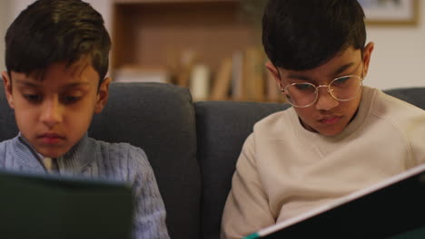 two young boys sitting on sofa at home playing games or streaming onto digital tablets 19