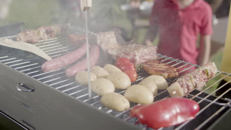 Man-turning-over-potatoes-with-meat-fork-on-barbecue-grill