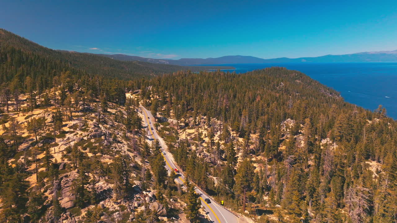 Rising over the mountainous landscape covered with pine tree forest. Road through the wood in the rocks. Blue lake at the foot of mountains.