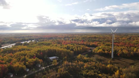 Autumn-forest-landscape,-small-homes-and-wind-turbine,-aerial-orbit-view