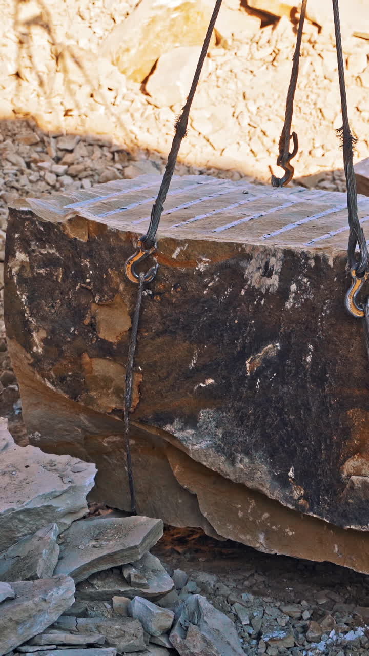 Crane lifting heavy rock. Heavy natural granite stone blocks stacked for processing Vertical video