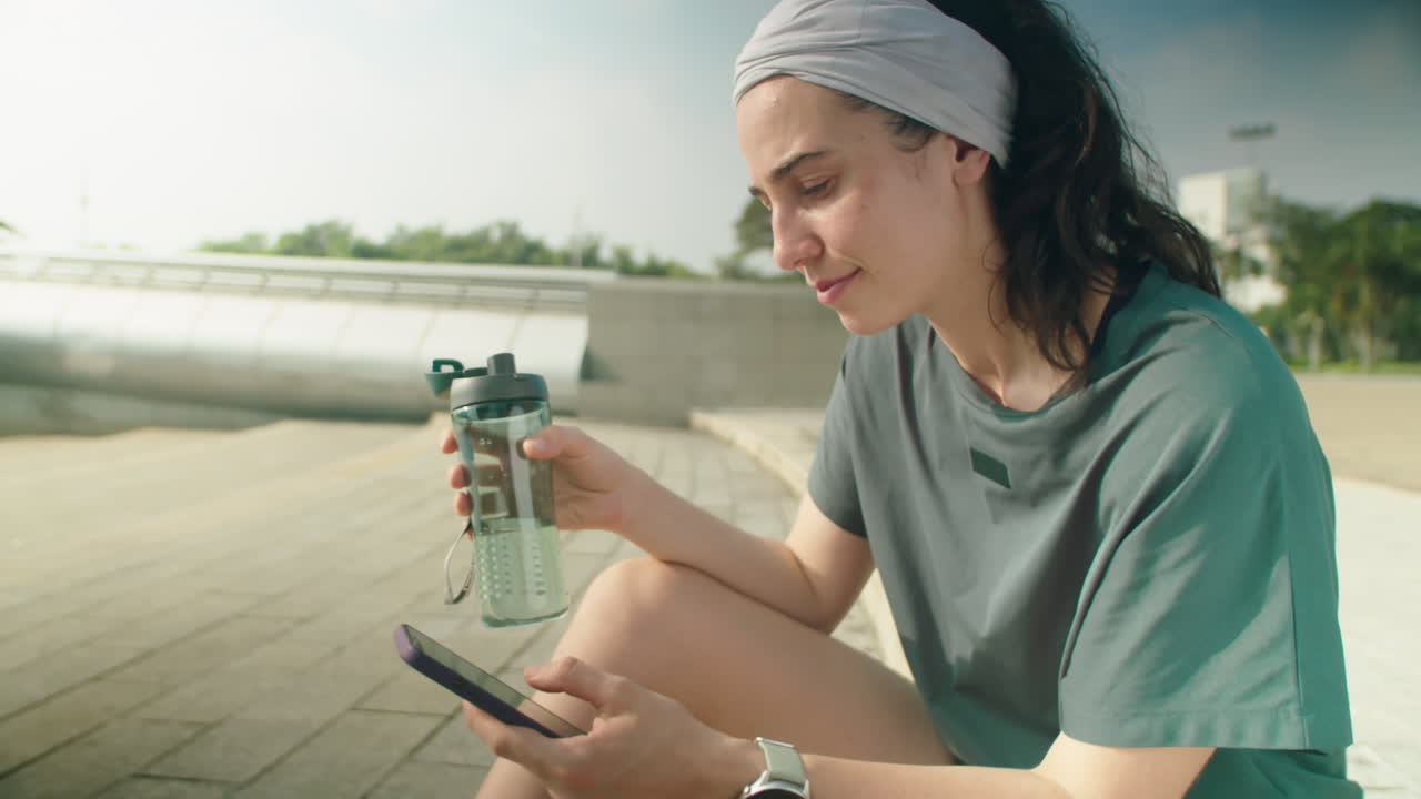 Woman Drinking Water and Using Phone after Running