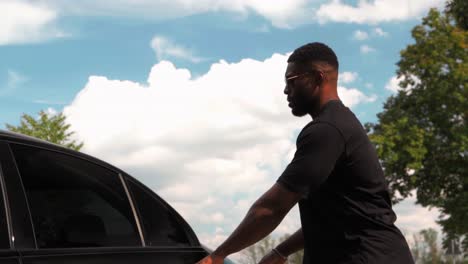 Stylish-Muscular-African-Man-Getting-Out-of-Car-Driver's-Seat-and-Takes-Backpack-Bag-from-Back-Seat---low-angle-tracking-in-slow-motion