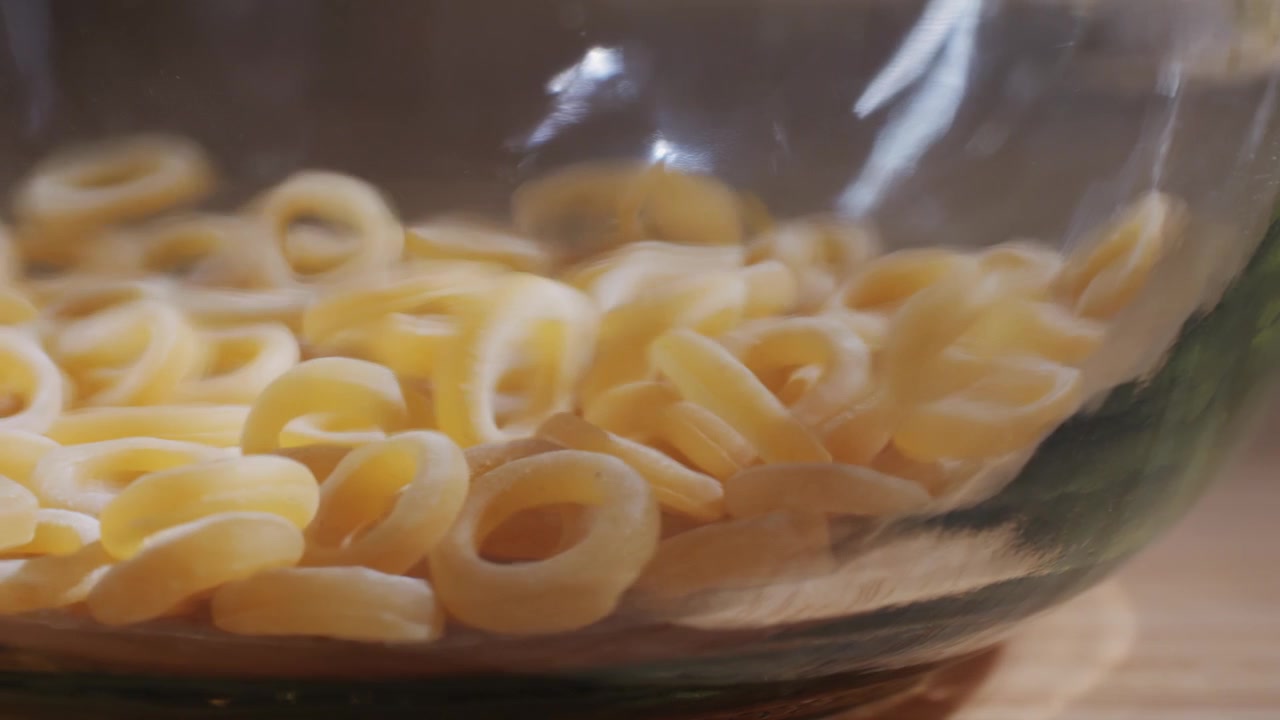 Pasta ad anello secca che cade in una ciotola di vetro