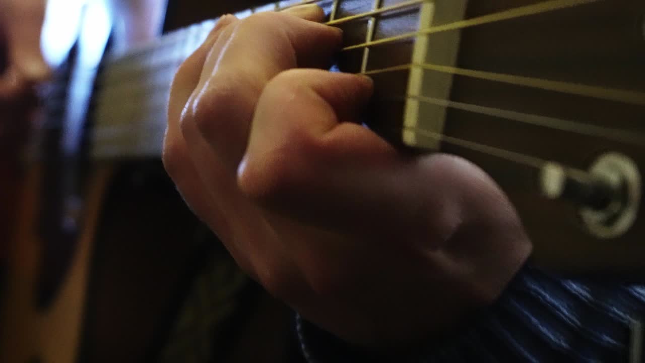 primer plano de las manos de un músico tocando varias notas en una guitarra electroacústica en su habitación