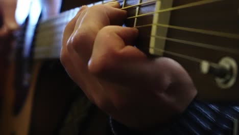 close-up of a musician's hands playing various notes on an electro-acoustic guitar in his room