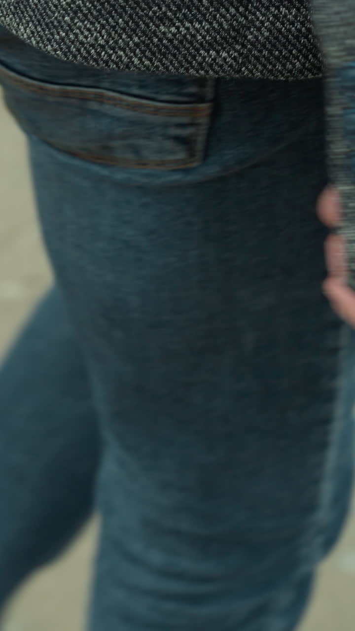 vista ravvicinata di una persona in giacca grigia, tela nera e jeans blu con una pistola al fianco, in piedi su una strada di terra, con uno sfondo sfocato