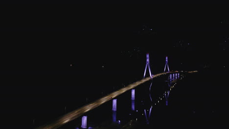 Drone-lights-flying-above-illuminated-bridge-above-water-at-night