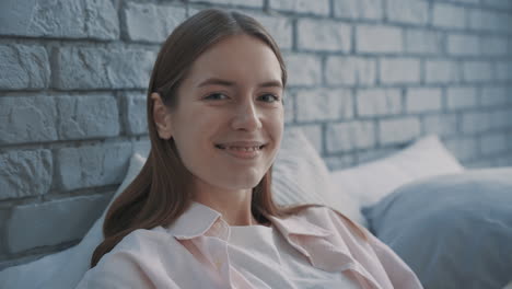 portrait of young pretty woman smiling and looking at camera sitting on the bed indoor