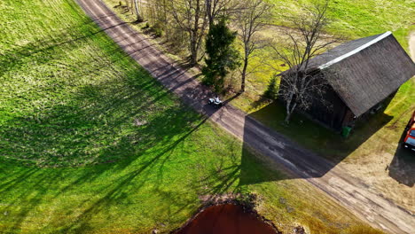 Drone follows a motorbike riding through countryside roads past a lake, barn, and open fields