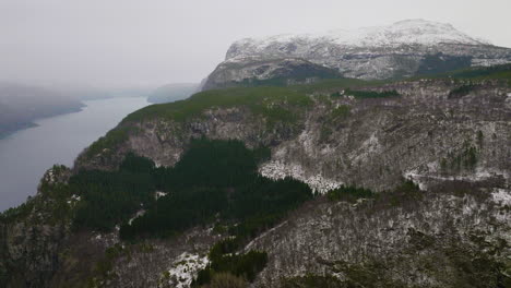 Fiordo-Brumoso-En-Paisaje-De-Montañas-Nevadas-Arbored-En-Noruega,-Antena