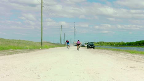 two bicyclists riding past camera dirt ride canal