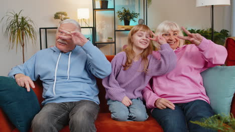 happy excited caucasian grandparents and granddaughter girl dancing together in disco style on sofa
