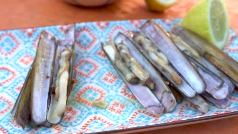 picking up the grooved razor shell by hand from the plate to eat