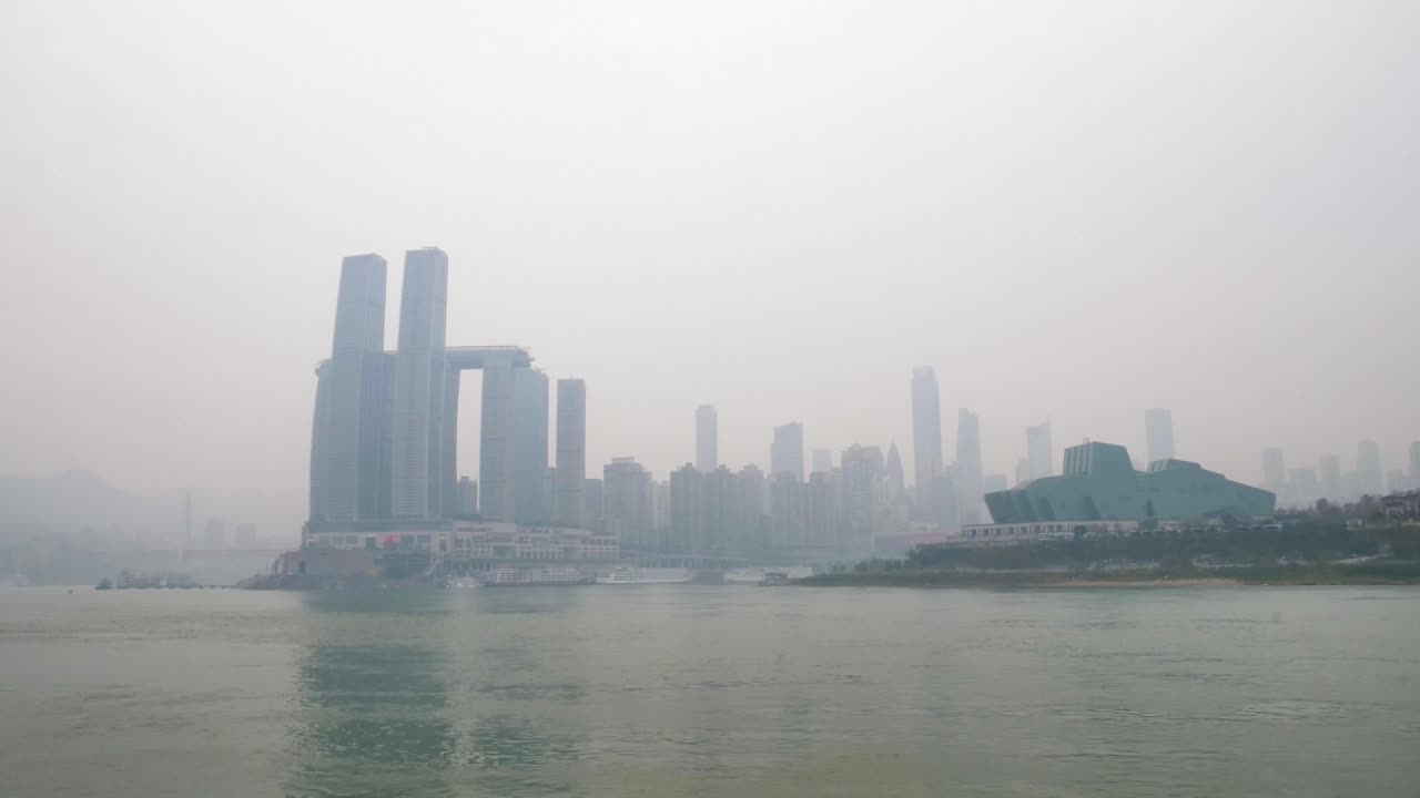 Hyperlapse of Chongqing’s skyline along the Yangtze River, showcasing modern skyscrapers and the iconic theater building, with a misty atmosphere over the cityscape. China