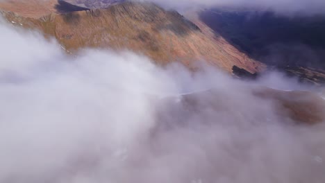 Drone-shot-pushing-forward-and-tilting-down-showing-clouds-rolling-off-a-mountain,-Helvellyn,-Lake-District,-Cumbria,-UK