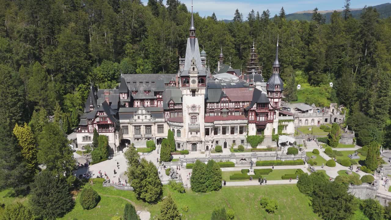 Drone orbiting around the historic Peleș Castle, highlighting its architecture and natural backdrop