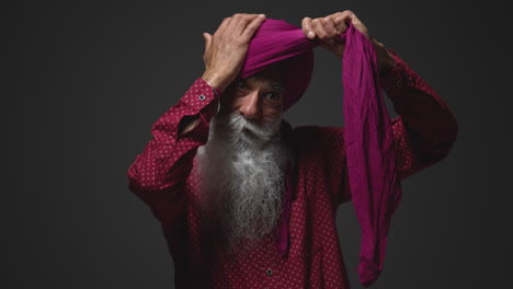 Fotografía-De-Estudio-Con-Iluminación-Tenue-De-Un-Hombre-Sikh-Mayor-Con-Barba-Atando-Una-Tela-Para-Un-Turbante-Contra-Un-Fondo-Oscuro,-Filmada-En-Tiempo-Real-2