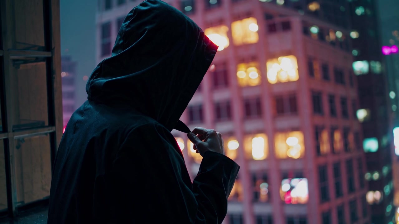 Person in Hooded Jacket Looking Out at City Skyline at Night