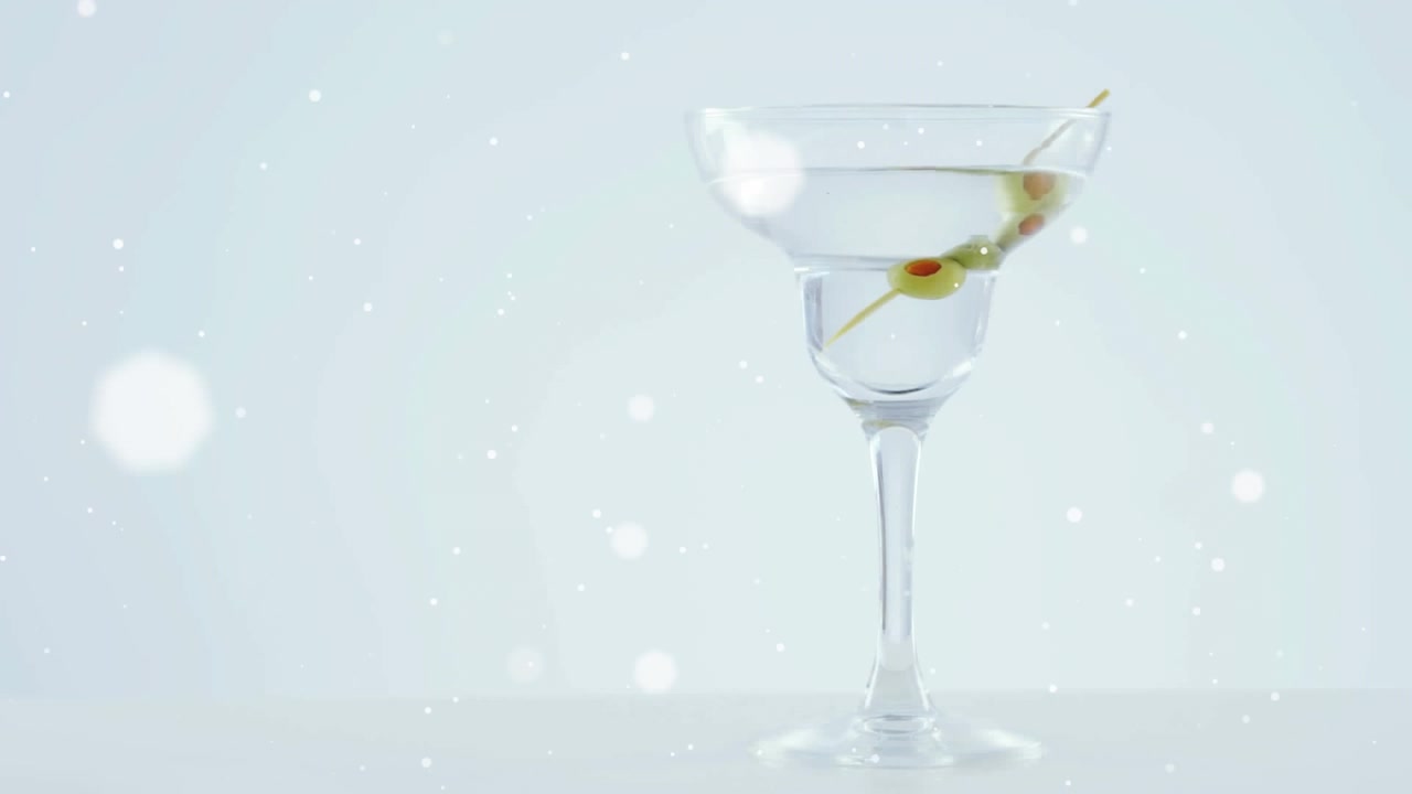 Macchie bianche che fluttuano su olive che cadono in un bicchiere da cocktail su sfondo grigio