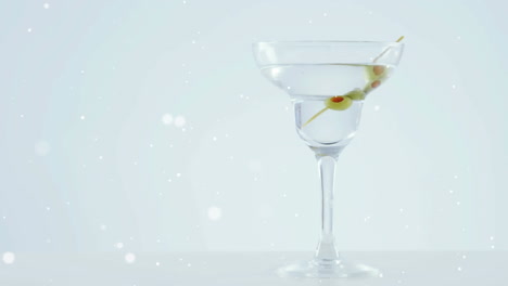 white spots floating over olives falling into cocktail glass against grey background