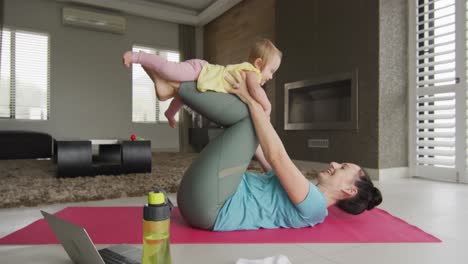 Kaukasische-Mutter-Spielt-Mit-Ihrem-Baby,-Während-Sie-Zu-Hause-Yoga-Auf-Einer-Yogamatte-Praktiziert