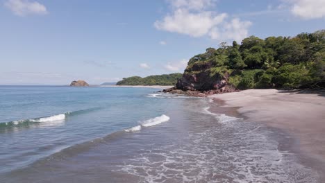 Low-Flyover-Of-Waves-Crashing-Below-Towards-A-Rocky-Hill