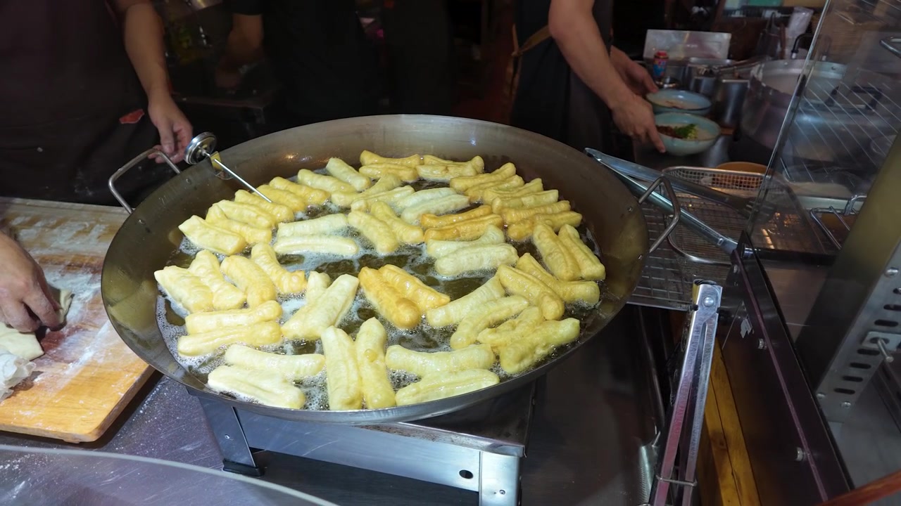 Primo piano di bastoncini di pasta dorati che friggono in olio bollente all'interno di un grande wok di metallo.